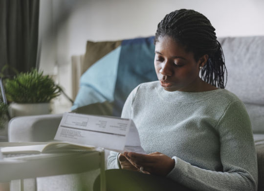 Portrait of a young African American businesswoman reading a utility bill while working remotely from home.