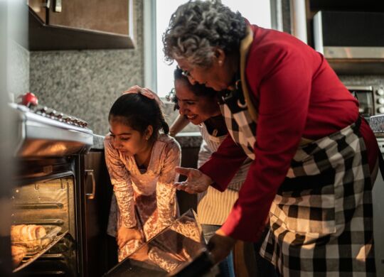 Grandmother, mother and daughter looking at food in the oven at home